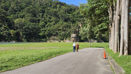 Taipei City, Taiwan. November 15, 2025. Tree-lined riverside walkway in Xindian couple people strolling through calm eco greenery on a bright relaxing day