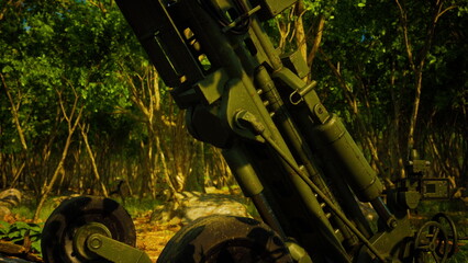 A large artillery system stands tall amid lush greenery. Sunlight filters through trees, creating a contrasting backdrop for this imposing piece of military equipment in action.