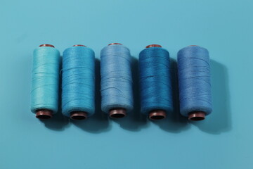 Set of different colorful sewing threads on light blue background, flat lay. With space for text.