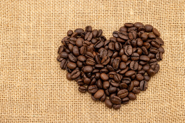 Roasted coffee beans in a heart shape on a sack of coffee background , with copy space , top view