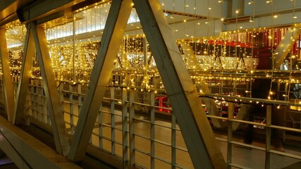 Timelapse Person Walking Through Illuminated Bridge Passage: Motion Blur Figure on Modern Walkway with Golden String Lights Night Scene - Powered by Adobe