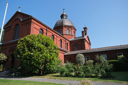 Exterior View of Historic Red Brick St Lawrence Church with Copper Dome and Green Shrubs in Foreground on a Sunny Day, Petersfield, Hampshire