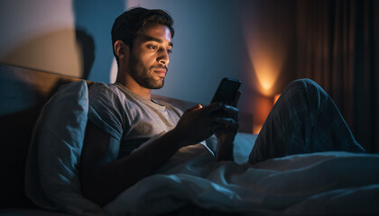 A man in bed, illuminated by the glow of his smartphone screen, late at night.