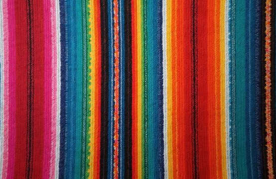 Vibrant vertical stripes of a serape or zarape textile in various colors like red, pink, blue, yellow, and green. Close up view of the woven fabric texture.