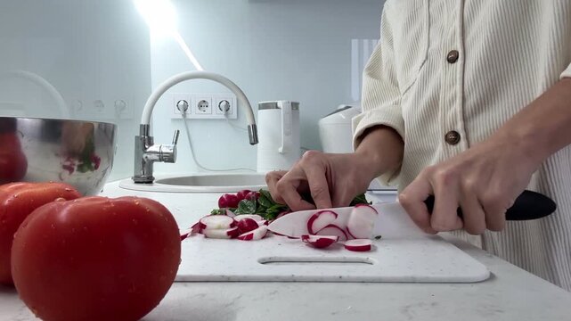Woman Slicing Fresh Radishes in Modern Minimalist Kitchen &ndash; Healthy Home Cooking Scene with Tomatoes and White Cutting Board