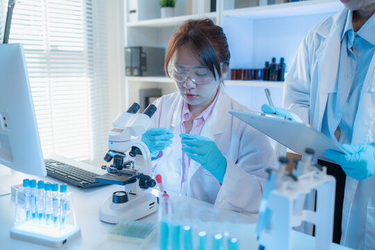 Two female scientists in white lab coats working together in a bright laboratory with microscopes, glassware, and blue test tubes, representing teamwork and modern scientific research environment. - Powered by Adobe