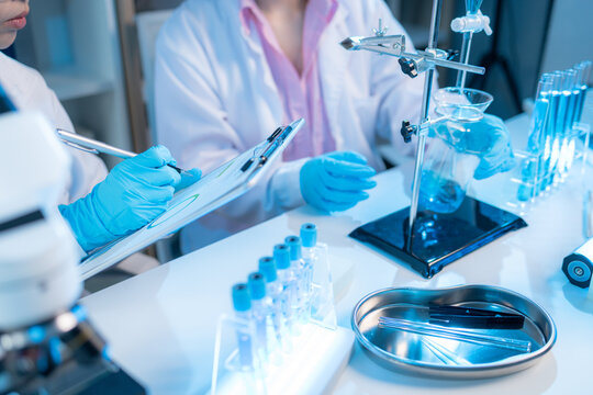 Two chemists in white lab coats working together in a modern laboratory surrounded by scientific equipment, computers, and glassware, representing teamwork in scientific research.