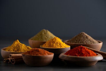 Assorted spices in wooden bowls against a dark gray background culinary photography