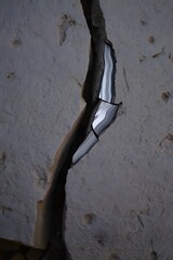 Crack in wall with peeling paint and plaster revealing shiny material underneath it
