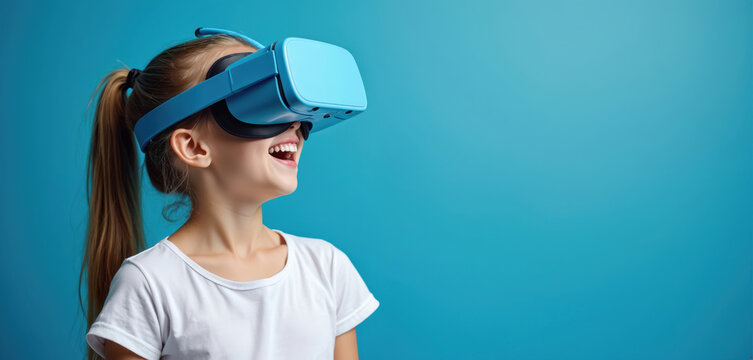 Happy girl wears blue virtual reality headset against blue background. Cheerful child laughs looking in vr goggles. Kid exploring digital world. Future tech fun for children entertainment.
