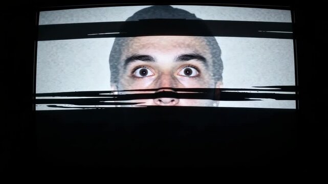 Terrified man's face emerging from static on an old television screen in a dark room. Composite sequence with glitch distortion representing fear, surveillance or media control