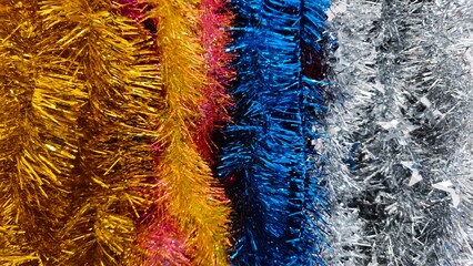 Vibrant tinsel decorations in gold, red, blue, and silver create a festive and sparkling texture. This colorful close-up is perfect for holiday promotions, event posters, party ads, gift shop catalogs