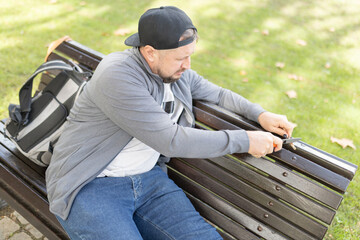 Man whittling wood with knife on park bench