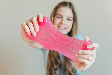 Close-up of hands stretching bright pink slime towards the camera, with a smiling girl in the background. Sensory toy