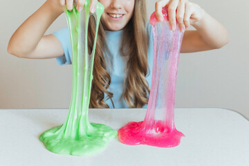 Girl stretching bright green and pink slime simultaneously, showcasing two colors. Fun dual sensory play activity