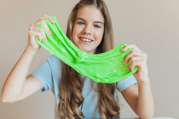 Smiling girl stretches wide a blob of vibrant neon green slime. Fun sensory toy and creative anti-stress activity