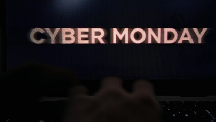 Hovering blurred hands moving over backlit laptop keyboard at desk, showing CYBER MONDAY text