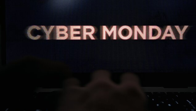 Hovering blurred hands moving over backlit laptop keyboard at desk, showing CYBER MONDAY text