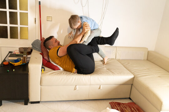 Father and son playing, wrestling on living room sofa - Powered by Adobe