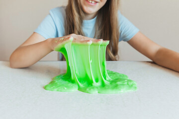 Smiling girl holding and stretching lime green slime wide, showcasing its elasticity and stringy texture. Fun sensory play