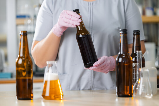 Worker chemist in brewery lab holding beer bottle with various brewing equipment - Powered by Adobe