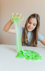 Smiling girl holding and stretching lime green slime wide, showcasing its elasticity and stringy texture. Fun sensory play