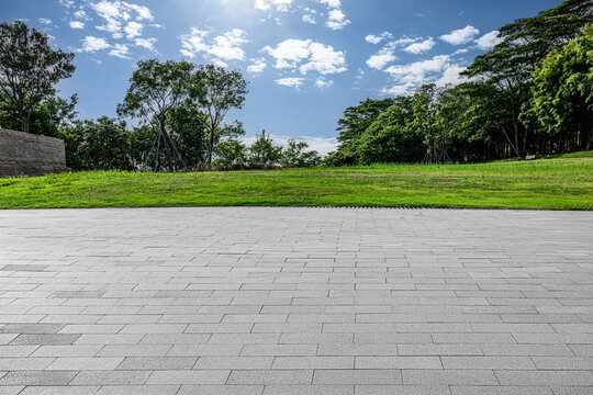 Empty square floor and green grass field with trees under blue sky clouds background.