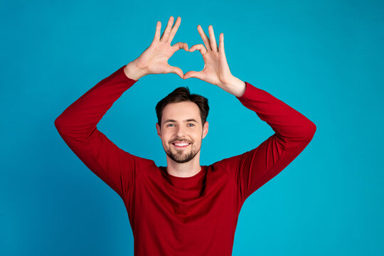 Smiling young man in red sweater forms heart shape with his hands against blue background for fashion lifestyle advertising - Powered by Adobe