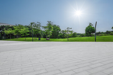 Empty square floor and green grass field with trees under blue sky sun background.
