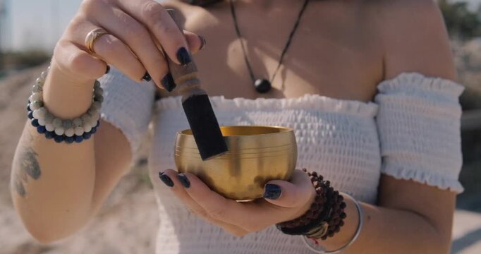 Close up woman begins to play Tibetan bowl with wooden mallet, representing sound healing and meditative focus. Concept of energy of mindfulness and the soothing vibration of inner calm