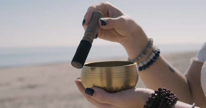 Close up woman begins to play Tibetan bowl with wooden mallet, representing sound healing and meditative focus. Concept of energy of mindfulness and the soothing vibration of inner calm