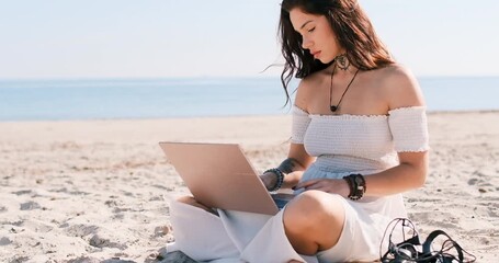 Woman sits on sandy beach, working on laptop under clear blue sky, completing her tasks, closes laptop, enjoy calm sense of accomplishment and sunny weather. Remote work, productivity and relaxation