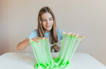 Smiling girl holding and stretching lime green slime wide, showcasing its elasticity and stringy texture. Fun sensory play