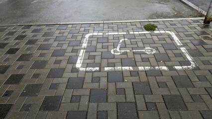 Designated scooter parking space on cobblestone pavement with white outline and greenery