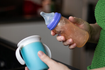 Close up of female hands holding a bottle and a no spin cup for baby milk