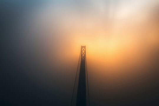 Fog envelops bridge structure at dawn with warm hues illuminating the scene - Powered by Adobe