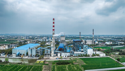 Aerial view of a large industrial factory with a smoking chimney located on the outskirts of a rural town.