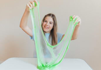 Girl stretching bright neon green slime into a thin translucent sheet on the table. Fun sensory and creative DIY hobby