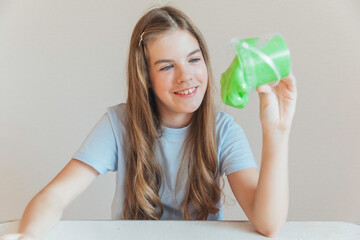 Smiling girl pouring vibrant green slime from a container onto the table. Trendy DIY and fun sensory play activity