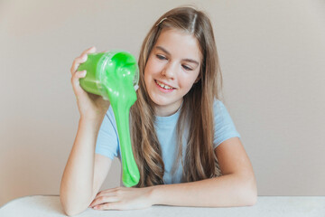 Smiling girl pouring vibrant green slime from a container onto the table. Trendy DIY and fun sensory play activity