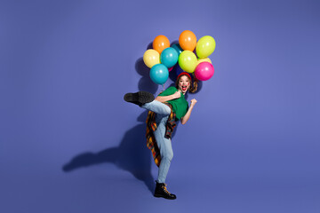 Young girl with colorful balloons jumps in the air smiling against purple backdrop to convey fun...