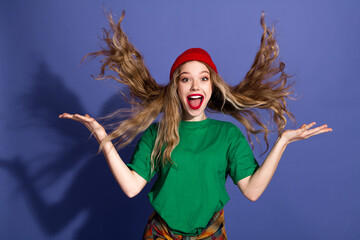 Young woman in red beanie green shirt leaps with joy hair flying against purple background for a...