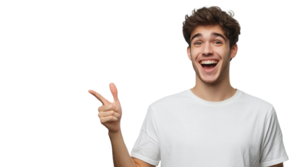 Young man smiles broadly and points to the side in a cheerful manner on a plain white background.