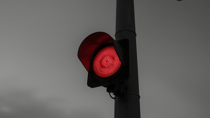 A red traffic light glows brightly against a desaturated background, indicating stop.