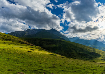 Green Pyrenees mountains with sun rays breaking through clouds
