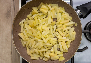 Potatoes cut into slices are deliciously fried in a frying pan.
