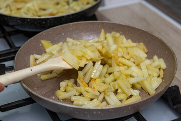 Potatoes cut into slices are deliciously fried in a frying pan.