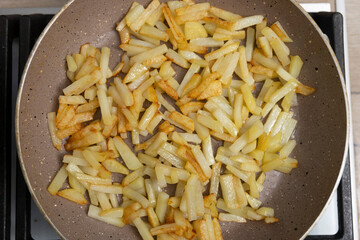 Potatoes cut into slices are deliciously fried in a frying pan.