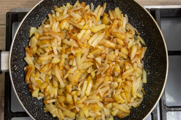 Sliced potatoes with onions are deliciously fried in a frying pan.