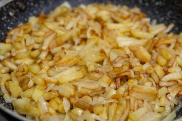 Sliced potatoes with onions are deliciously fried in a frying pan.